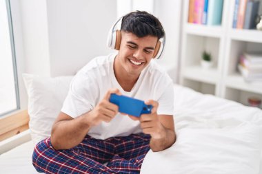 Genç İspanyol adam gülümsüyor. Yatak odasında oyun oynarken kendine güveniyor.