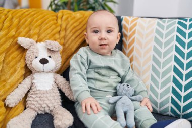 Evdeki bebeklerle kanepede oturan sevimli beyaz bebek.