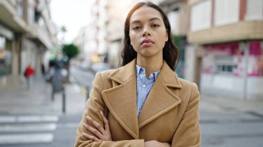 Ciddi bir ifadeyle duran ve caddede kollarını kavuşturan genç, güzel İspanyol kadın.