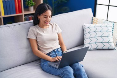 Evdeki kanepede dizüstü bilgisayar kullanan güzel İspanyol kadın.