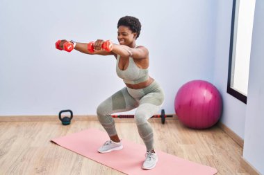 Afrikalı Amerikalı kadın gülümsüyor spor merkezinde halterleri kullanarak antrenman yapıyor.