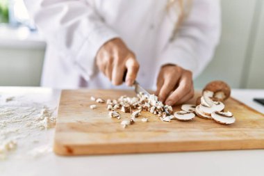 Young woman wearing cook uniform cutting mushrooms at kitchen