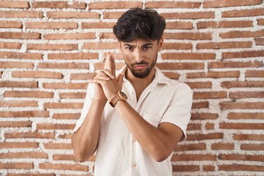 Duvarın arkasında duran sakallı bir Arap. Elinde el hareketleriyle sembolik bir silah tutuyor. Cinayet silahlarıyla oynuyor. 