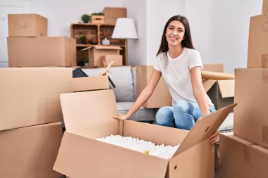 Genç, güzel, İspanyol bir kadın gülerek yeni evindeki karton kutuları açıyor.