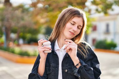 Young blonde woman listening to music and dancing at park