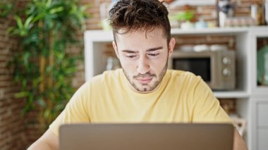 Yemek odasındaki masada dizüstü bilgisayar kullanan genç bir İspanyol.