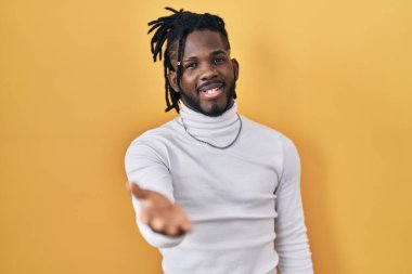 Sarı arka planda balıkçı yaka kazak giyen Afrikalı bir adam gülümseyen bir avuç içi kadar yardım ve kabul görüyor.. 