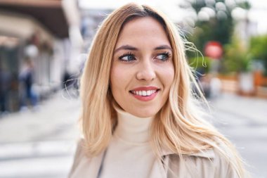 Young blonde woman smiling confident looking to the side at street