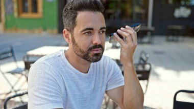 Genç İspanyol adam akıllı telefondan sesli mesaj dinliyor kahve dükkanının terasında oturuyor.