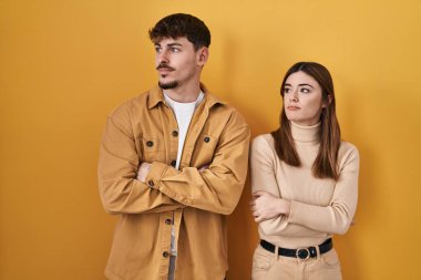 Sarı arka planda duran genç İspanyol çift kollarını kavuşturmuş, ikna olmuş ve kendinden emin bir şekilde yan tarafa bakıyor. 