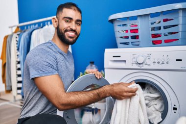 Çamaşır odasında kendine güvenen genç İspanyol adam gülümsüyor.