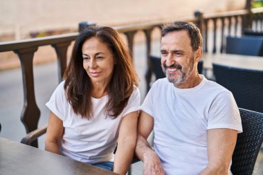 Middle age man and woman couple sitting on table at coffee shop terrace