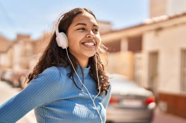 Genç Afro-Amerikalı kadın gülerek sokakta müzik dinliyor.