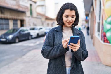 Sokakta akıllı telefon kullanan kendine güvenen genç bir kadın.