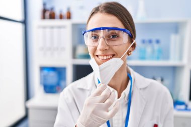 Laboratuvarda tıbbi maske takan beyaz kadın bilim adamı.