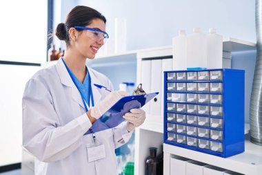 Young beautiful hispanic woman scientist writing report working at laboratory