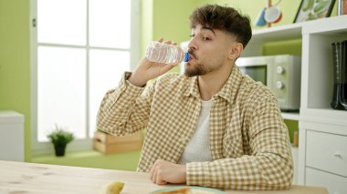 Genç Arap adam evdeki masada oturmuş su içiyor.