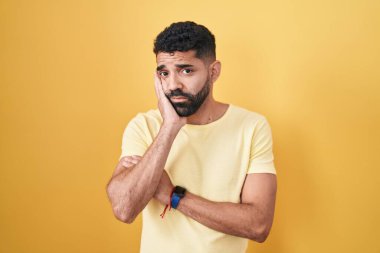 Sarı arka planda duran İspanyol sakallı adam çapraz kollu depresyon sorunlarından yorgun ve sıkılmış göründüğünü düşünüyor.. 