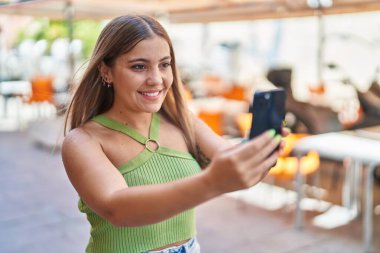 Young beautiful hispanic woman smiling confident making selfie by the smartphone at coffee shop terrace