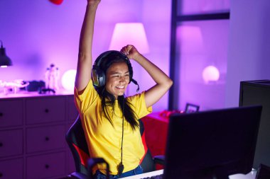 Genç, güzel, Latin bir kadın oyuncu oyun odasında video oyunu oynuyor.