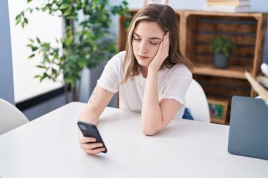 Young woman using smartphone sitting on table at home