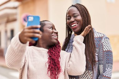 Afro-Amerikalı kadın arkadaşlar, sokakta video araması yaptıkları için gülümsüyorlar.