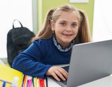 Sınıftaki masada dizüstü bilgisayar kullanan sevimli sarışın kız öğrenci.
