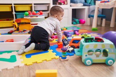 Anaokulunda yerde oturan sevimli İspanyol çocuk araba oyuncağıyla oynuyor.