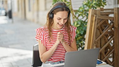 Laptop ve kulaklık kullanan genç sarışın kadın kahve dükkanının terasında birinci sınıf bir jest yaptı.