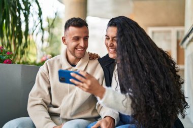 Man and woman smiling confident watching video on smartphone at street