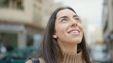 Young beautiful hispanic woman smiling confident looking to the sky at street