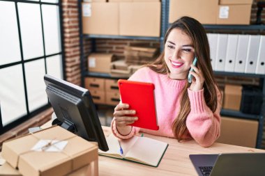 Genç ve güzel bir İspanyol kadın. İş kadını. Ofiste akıllı telefondan konuşan bir dokunmatik ped kullanıyor.