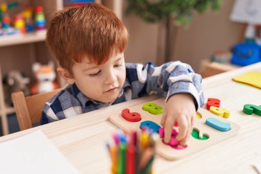 Sınıftaki masada oturan, matematik bilmecesiyle oynayan sevimli çocuk.