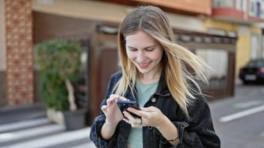 Kafe terasında gülümseyen akıllı telefon kullanan genç sarışın kadın.