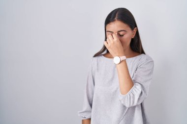 Young hispanic woman standing over white background tired rubbing nose and eyes feeling fatigue and headache. stress and frustration concept. 