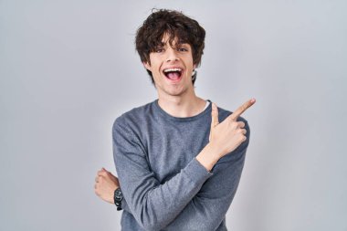 İzole edilmiş arka planda duran genç adam yüzünde kocaman bir gülümsemeyle, kameraya el ile işaret ederek bakıyor.. 