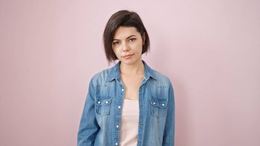 Soyutlanmış pembe arka planda ciddi bir ifadeyle duran beyaz bir kadın.
