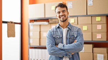 Young hispanic man ecommerce business worker standing with arms crossed gesture at office