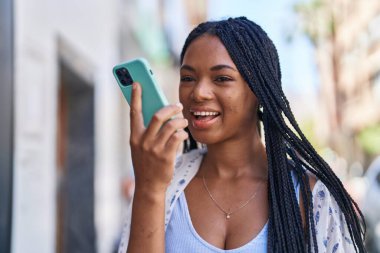 Afro-Amerikalı kadın gülümsüyor. Akıllı telefondan konuşuyor.