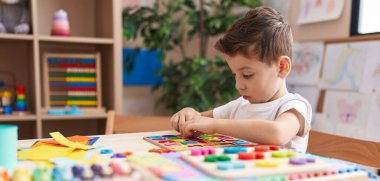 Anaokulunda masada oturmuş matematik oyunu oynayan sevimli beyaz çocuk.
