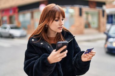 Sokakta akıllı telefon ve kredi kartı kullanan genç bir kadın.