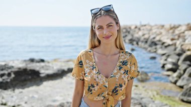 Young blonde woman smiling confident standing at seaside