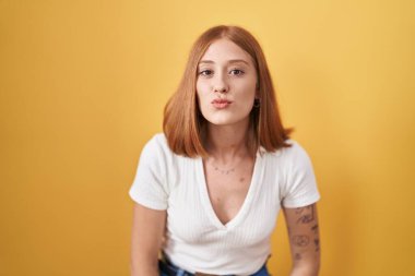 Sarı arka planda duran genç kızıl saçlı kadın, canlı yayında öpüşürken kameraya bakıyor. Sevimli ve seksi. aşk ifadesi. 