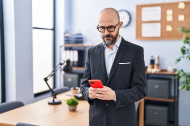 Genç kel iş adamı ofiste akıllı telefon kullanıyor.