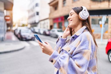 Genç, güzel, İspanyol bir kadın sokakta müzik dinliyor.