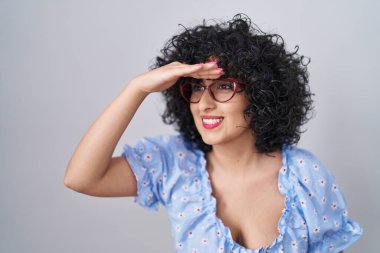 Kıvırcık saçlı, gözlüklü, izole edilmiş arka planda mutlu ve tebessüm eden genç esmer bir kadın. arama kavramı. 