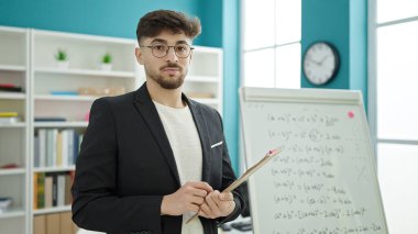 Üniversite sınıfında rahat bir ifadeyle duran genç Arap erkek öğrenci.