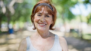Orta yaşlı bir kadın parkta kendine güvenerek gülümsüyor.
