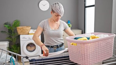 Çamaşır odasında çamaşır ipine elbise asan genç bir kadın.