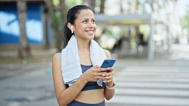 Young beautiful hispanic woman wearing sportswear using smartphone at street